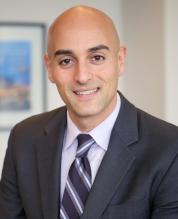 Adam Mostafa, Managing Director of Banking and Investor Relations, smiling in a suit and tie in a professional office setting.