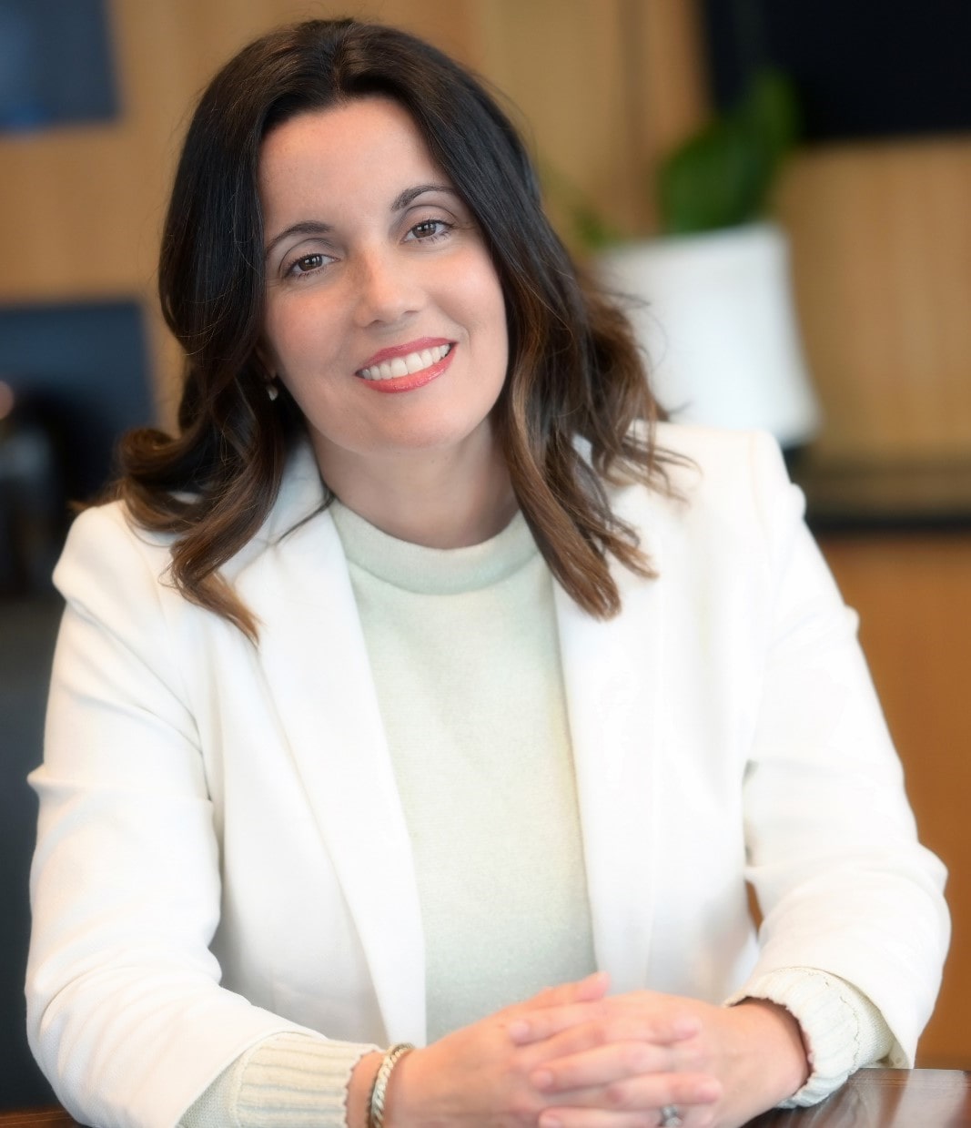 Ines Macias-Perez, Ph.D., Director of Product Development, smiling while seated at a table in a professional office environment.